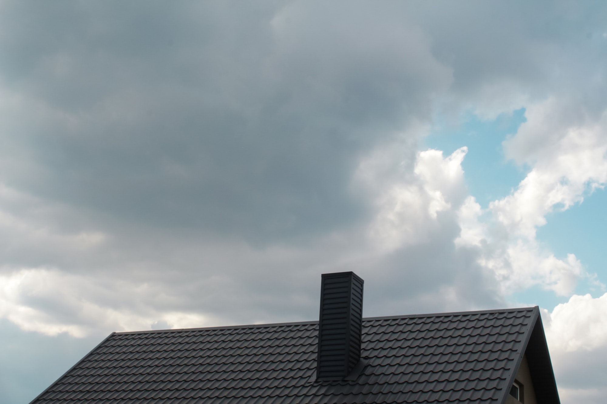 steel roof on dark sky background. Dark rain clouds above the modern roof. Roof with new black roofi